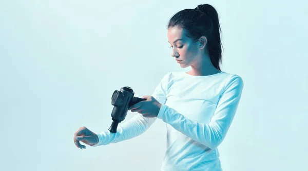 Αθλητική νεαρή γυναίκα μασάζ χέρι με το χέρι όπλο μασάζ σε νέον φως, μετά την προπόνηση ρουτίνες αποκατάστασης — Φωτογραφία Αρχείου