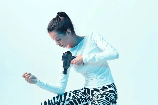 Masajeador de percusión, atlético joven morena mujer masaje de la mano en neón estudio de luz — Foto de Stock