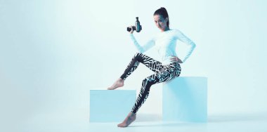 Perküsyon masajcısı, atletik esmer kadın neon stüdyo ışığı altında eklem ağrısı giderici için masaj silahı gösteriyor.