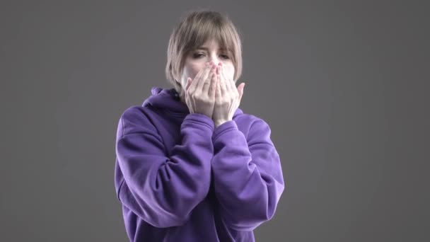 Linda chica caucásica joven en sudadera con capucha frota las manos tratando de mantener el calor en el fondo gris estudio — Vídeo de stock