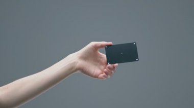 Kadın eli, gri stüdyo arka planında izleme noktaları olan siyah plastik bir banka kartı gösteriyor.