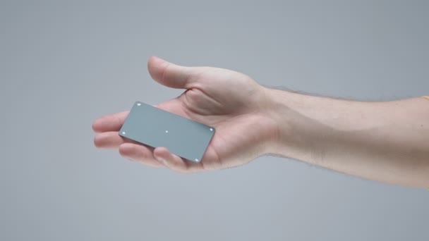 Schwarze Plastikkreditkarte fällt in männliche Handfläche auf grauem Studiohintergrund — Stockvideo