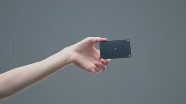 Gri stüdyo arka planında izleme noktaları olan siyah plastik bir banka kartı gösteren bir kadın el.