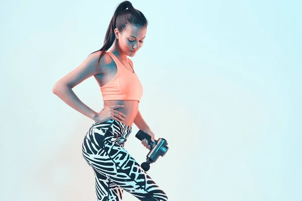 Atletik, genç bayan, el bilgisayarı ile masaj yapıyor. Kas gevşemesi için masaj yapıyor. Egzersiz yaptıktan sonra iyileşiyor.