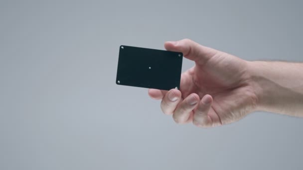 Mužská ruka zobrazující černou plastovou bankovní kartu se sledovacími body na šedém pozadí studia, reklamní video — Stock video