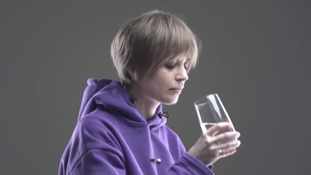 Современная коротковолосая молодая девушка пьет минеральную воду в стеклянном утоляющем жажду теле, медицинская рутина, 4k видео — стоковое видео