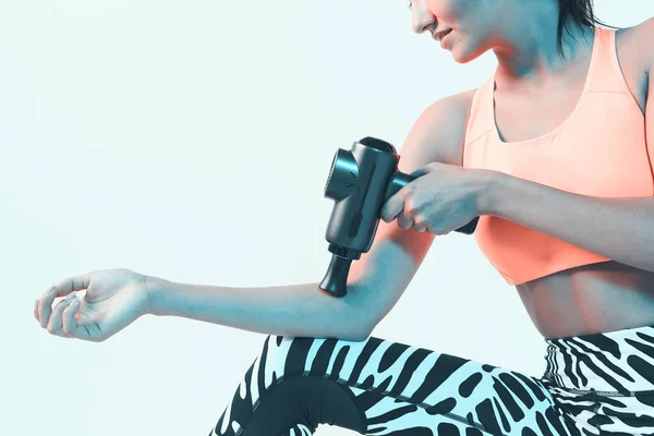 Спортивная молодая женщина массирует руку ручным массажным пистолетом, после тренировки процедуры восстановления, крупным планом — стоковое фото