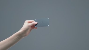 Kadın eli, gri stüdyo arka planında izleme noktaları olan siyah plastik bir banka kartı gösteriyor.