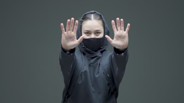 Жінка в чорній масці показує захисні жести рук і йде. Гендерно-дискримінаційний протест, боротьба за права жінок — стокове відео