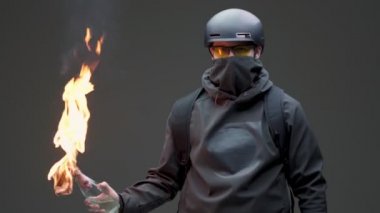 Siyah maskeli ve miğferli adam protestocu. Gri stüdyo arka planında isyan üzerine molotof kokteyli.
