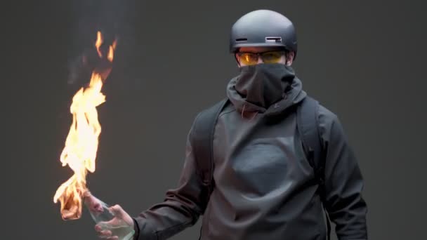 검은 마스크와 헬멧을 쓰고 회색 스튜디오 배경에서 폭동에 대한 화염병을 사용 한 가이 시위자 — 비디오