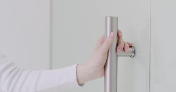 Kvinna bär vit polotröja touch metallic modern dörr handtag, tryck och in i rummet, närbild — Stockvideo