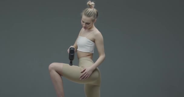 Athletische junge blonde Frau in Sportbekleidung massiert Bein durch Handheld-Perkussionsmassage, Erholung nach dem Training — Stockvideo