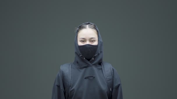 Colère rebelle asiatique fille en noir masque et sweat à capuche protestataire activiste posant sur gris studio fond — Video