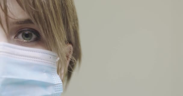 Blisko oko kobiety noszącej medyczną maskę twarzy patrzącej na kamerę z koronawirusem na szarym tle z przestrzenią do kopiowania — Wideo stockowe