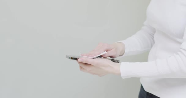 Жінка, що застосовує дезінфікуючий телефон під час прихованої пандемії на сірому фоні з копіювальним простором, крупним планом — стокове відео