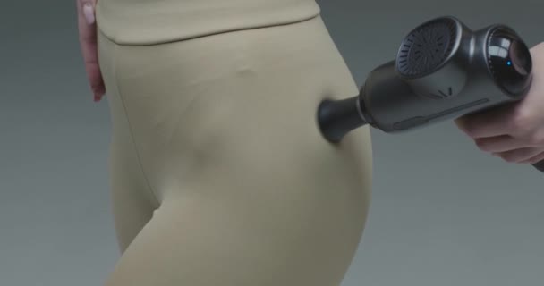 Primer plano de la mano femenina masajeando los músculos de la cadera por el masajeador de percusión sobre fondo gris estudio — Vídeo de stock