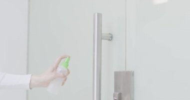 Kadınlar kapı kolunu dezenfektan sprey ve mendille temizler. Coronavirüs salgını sırasında ofis temizleme servisi, kapatın.