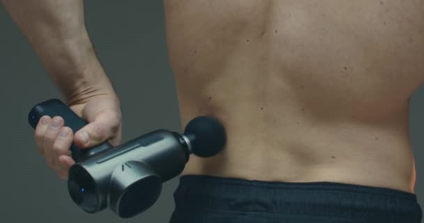 Atletisk kille massera nedre delen av ryggen med handhållen slagverk massage pistol för att lindra värk, närbild — Stockvideo