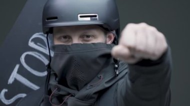 Siyah maskeli, karton posterli ve yazıt durduruculu beyaz bir adam. Yaklaş.