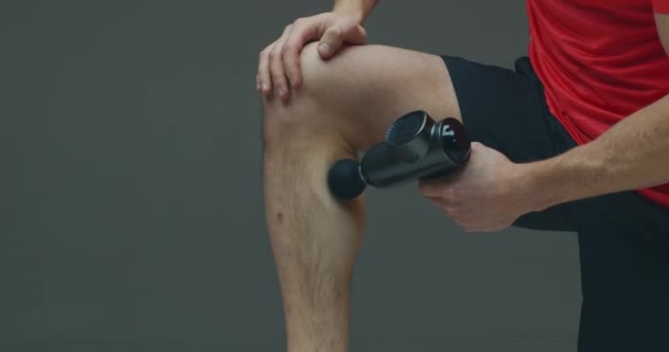 Перкусійний масажер, крупним планом спортсмен чоловічої масажної ноги за допомогою масажного пістолета в студії, передтренувальні розминки — стокове відео