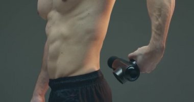 Derin doku perküsyon masaj aleti, atletik adam gri stüdyo arka planında ağrı kesici için sırt masajı yapıyor.