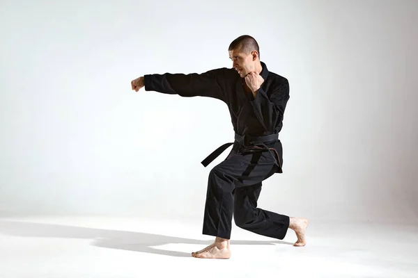 Fighting guy in black kimono fighter demonstrujące technikę karate na tle studio z miejsca kopiowania — Zdjęcie stockowe