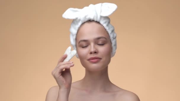 Krásná mladá dívka se zdravou pletí nosí bondáž na hlavě masáže obličeje podle gua sha jade kámen — Stock video
