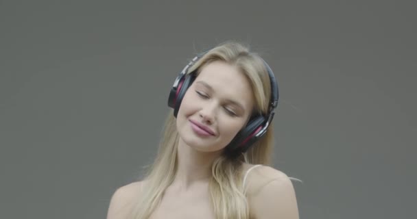 Tančící mladá krásná dívka v bezdrátových sluchátkách melomaniac poslouchat hudbu těší zvuk, zblízka na šedém pozadí — Stock video