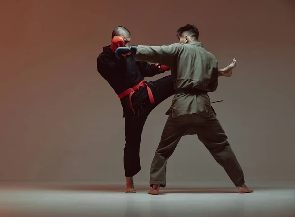 Wrestling of two fighting males in kimono and boxing gloves in red light in studio, martial arts, mixed fight concept — Stock Photo, Image