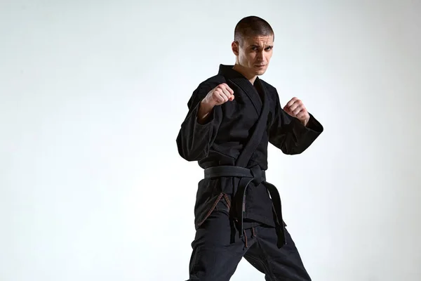 Selbstbewusster Mann im schwarzen Kimono-Kämpfer posiert in Karate-Haltung auf weißem Studiohintergrund mit Kopierraum — Stockfoto