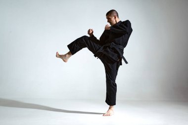 Siyah kimonolu dövüşçü, stüdyo arka planında Jiu Jitsu tekniği gösteriyor.