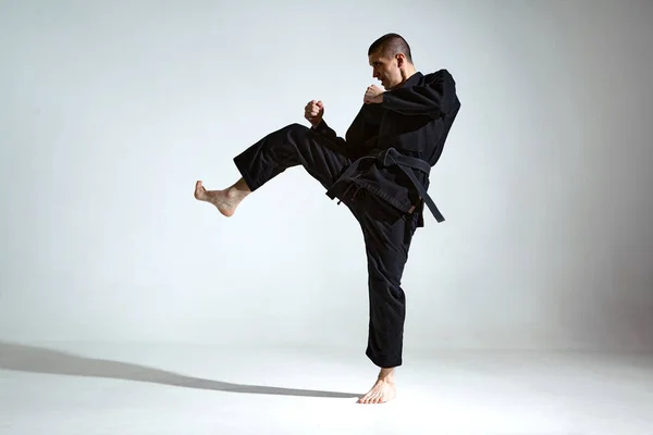 Fighting guy in black kimono fighter shows jiu jitsu technique on studio background with blank space, mix fight concept — Zdjęcie stockowe