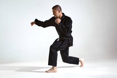 Siyah kimono dövüşçüsü spor eğitmeni stüdyo arka planında fotokopi alanı ile karate tekniği gösteriyor.