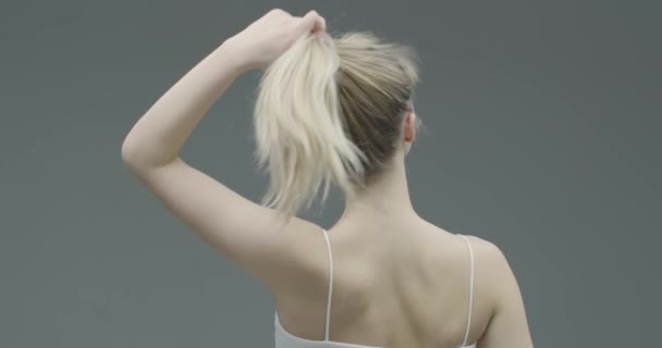 Гарненька молода блондинка знімає спанччі з волосся, задоволені пофарбованим станом волосся, ранкова рутина, вид ззаду — стокове відео