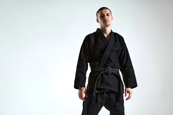 Cool guy in black kimono fighter posing in karate stance on white studio background with copy space — Stock Photo, Image