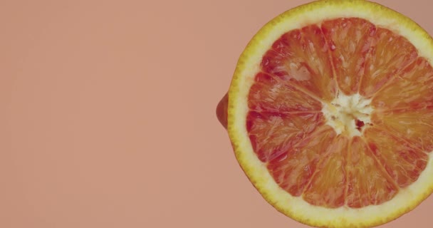 쥬스는 복제품 공간과 신선 한 맛있는 비타민을 갖춘 분홍색 스튜디오 배경에 있는 자연적 인 생체 오렌지 열매에 흘러들어간다 — 비디오