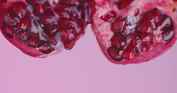 Juice flows on natural pomegranate fruit on pink studio background with copy space, healthy eating concept — Stock Video