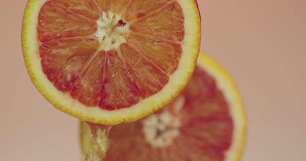 Δύο φυσικά πορτοκάλια, σταγόνες χυμού ρέει κάτω σε βιολογικά φρούτα σε ροζ φόντο στούντιο, φρέσκα νόστιμα βιταμίνες — Αρχείο Βίντεο