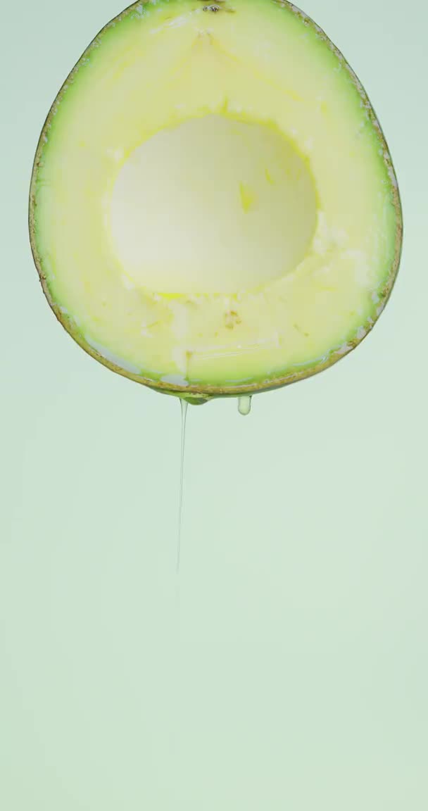 Olie druppels stromen op natuurlijke groene pitted avocado op studio achtergrond met kopieerruimte voor reclame, gezond eten concept — Stockvideo