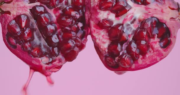 Сік падає вниз на органічні червоні гранатові фрукти на рожевому фоні студії, свіжі вітаміни, крупним планом — стокове відео