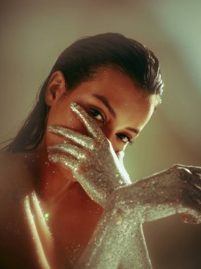 Gümüş parıldayan kadın elleri, ışıl ışıl parıldayan vücut sanatı ile poz veren genç kız, güzel yüzünü kol kola kapat.