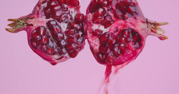 Saft fließt auf Hälften natürlicher roter Granatapfelfrüchte auf rosa Studiohintergrund, gesundes Ernährungskonzept — Stockvideo
