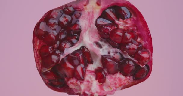 Suco derramando na fruta romã natural no fundo do estúdio rosa, close-up de vídeo, conceito de alimentação saudável — Vídeo de Stock