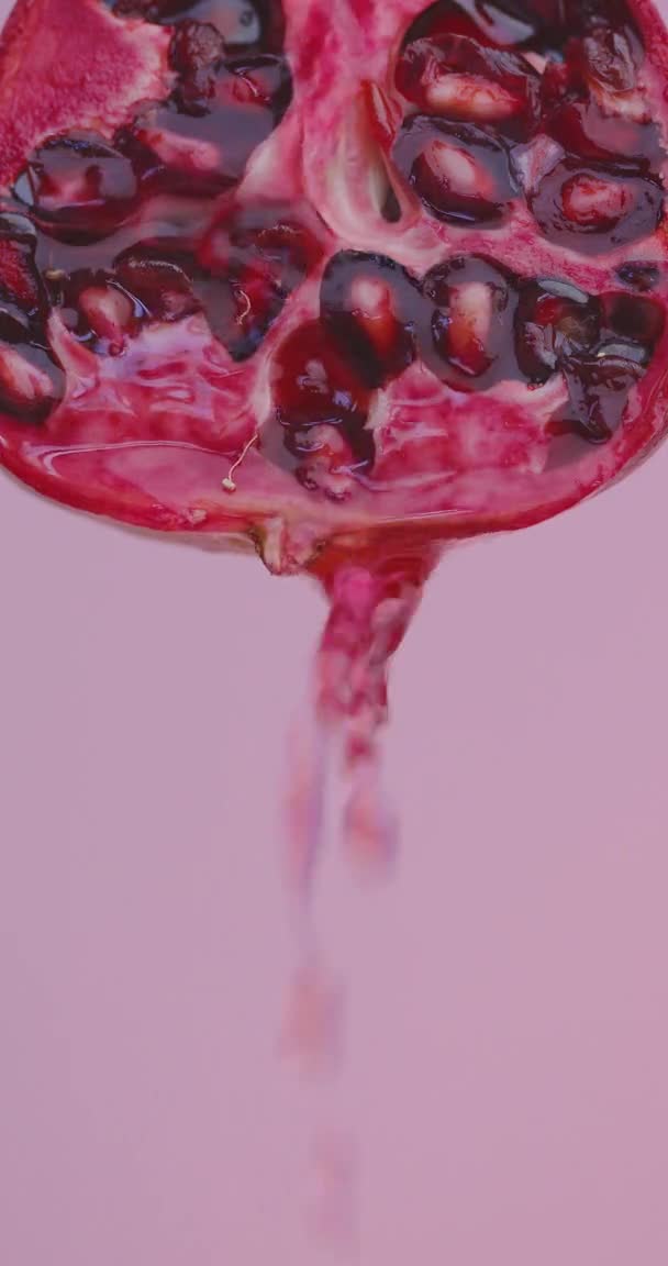 垂直ビデオ。ジュースの滴は、コピースペース、新鮮なビタミンとピンクのスタジオの背景に天然ザクロから流れ落ちます — ストック動画