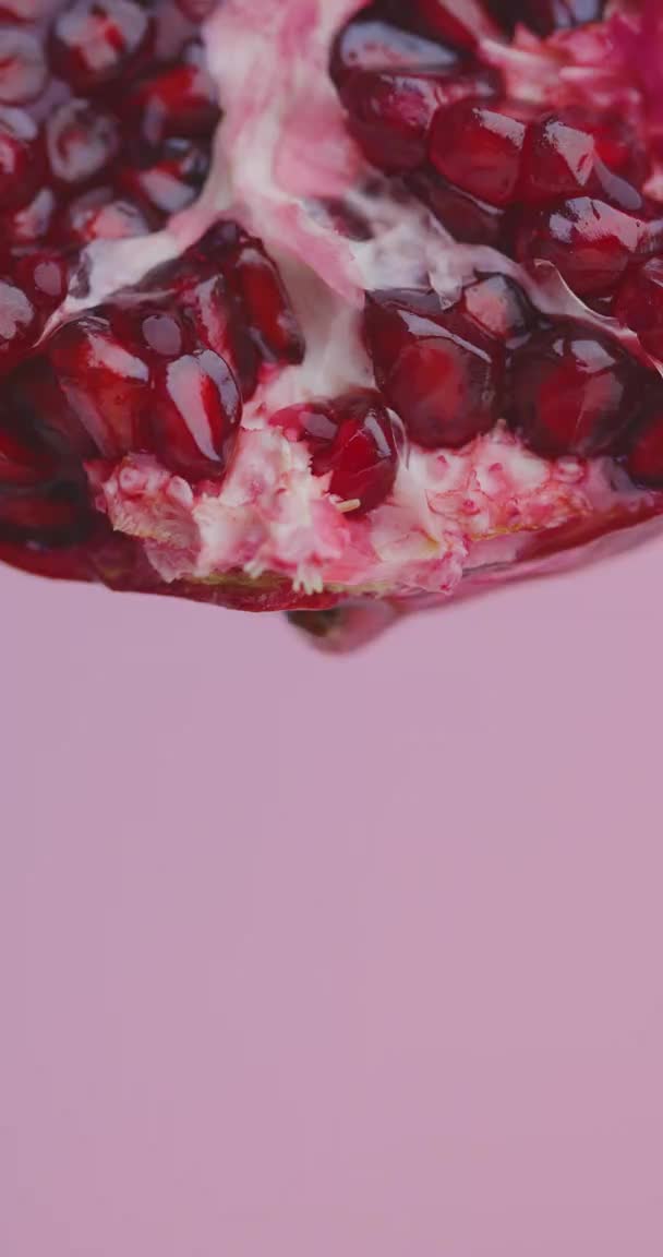 Verticale video. Sap druppels stroomt naar beneden van granaatappel fruit op roze studio achtergrond met kopieerruimte, verse vitaminen — Stockvideo