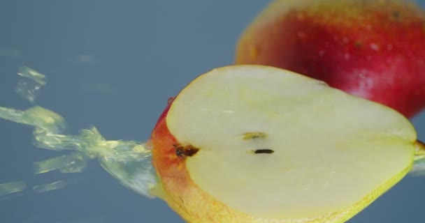 Vídeo vertical. Jugo de pera o limonada fluye hacia abajo de la fruta natural en el fondo del estudio azul, comida vegana, primer plano — Vídeo de stock