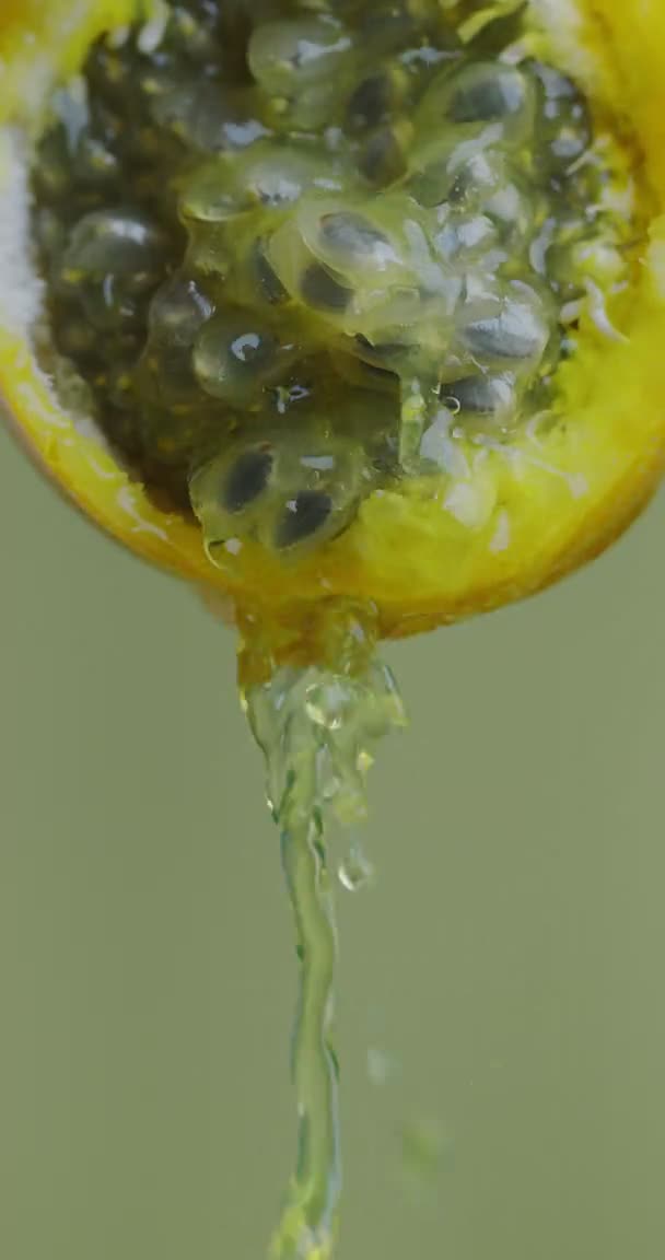 Vertikální video. Granadilla Šťáva nebo kapky vody tekoucí ze žluté exotické vášeň ovoce na zeleném pozadí studia — Stock video