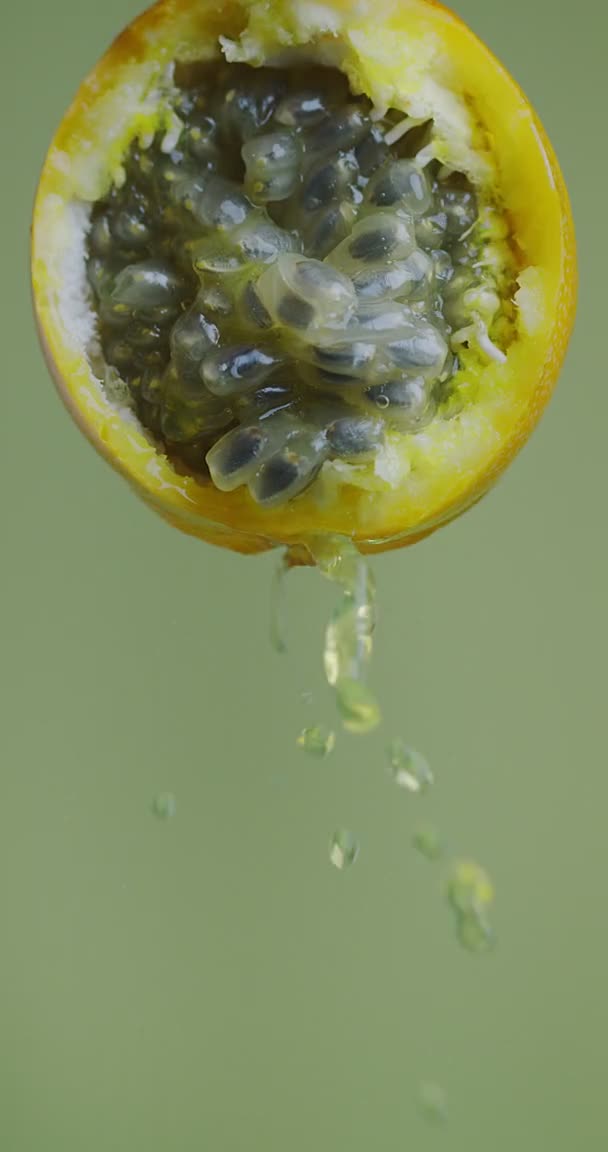 Vertikal video. Vatten stänk flöde ner från naturliga granadilla frukt på grön studio bakgrund med kopia utrymme — Stockvideo