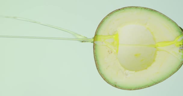 Verticale video. Oliedruppels stromen op natuurlijke bio groene pitten avocado op studio achtergrond met kopieerruimte voor advertentie — Stockvideo